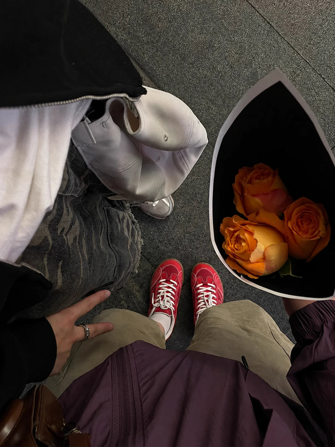 Overhead view of red racing-style sneakers with khaki trousers and a purple jacket beside a bouquet of orange roses.