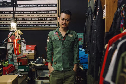 SBTG founder in workshop — olive utility shirt amid sneakers and streetwear