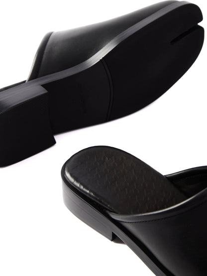 Close-up of black leather mules showing the split toe and stacked low heel on white background
