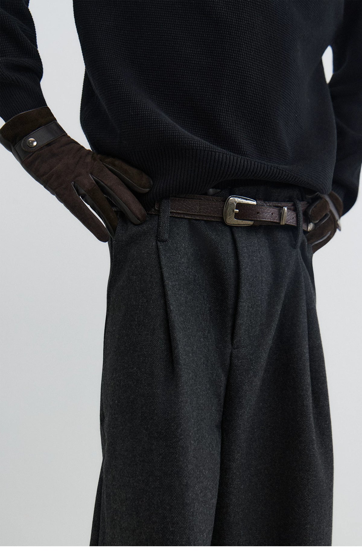 Black textured leather pin buckle belt worn with a black knit and pleated trousers