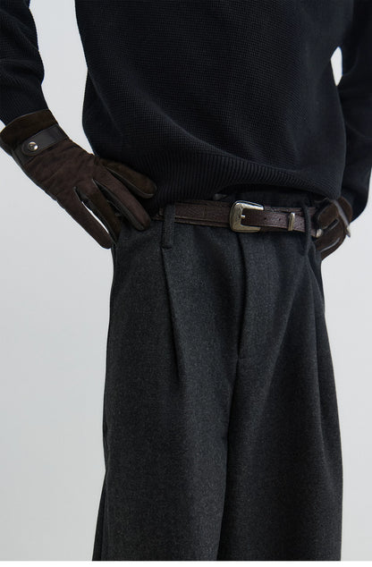 Black textured leather pin buckle belt worn with a black knit and pleated trousers