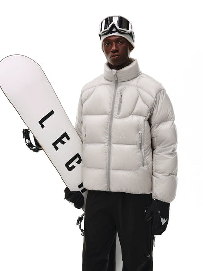 A person in an EastLyst Aurora Puffer Jacket, black snow pants, ski goggles, and gloves stands holding a white snowboard with bold black lettering against a plain white background.