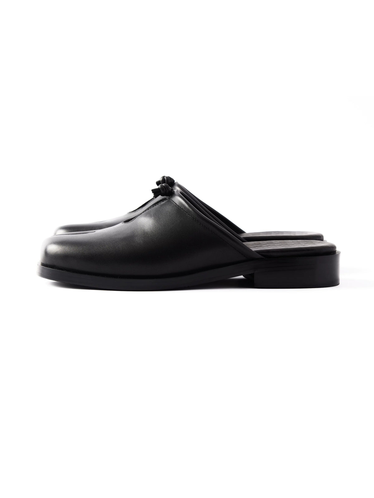 Black leather split-toe mule with knot detail, side profile showing open heel on white background