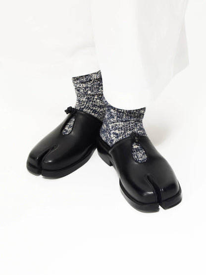 Black split-toe mules with knotted cutout worn with grey speckled socks, front angled view on white background