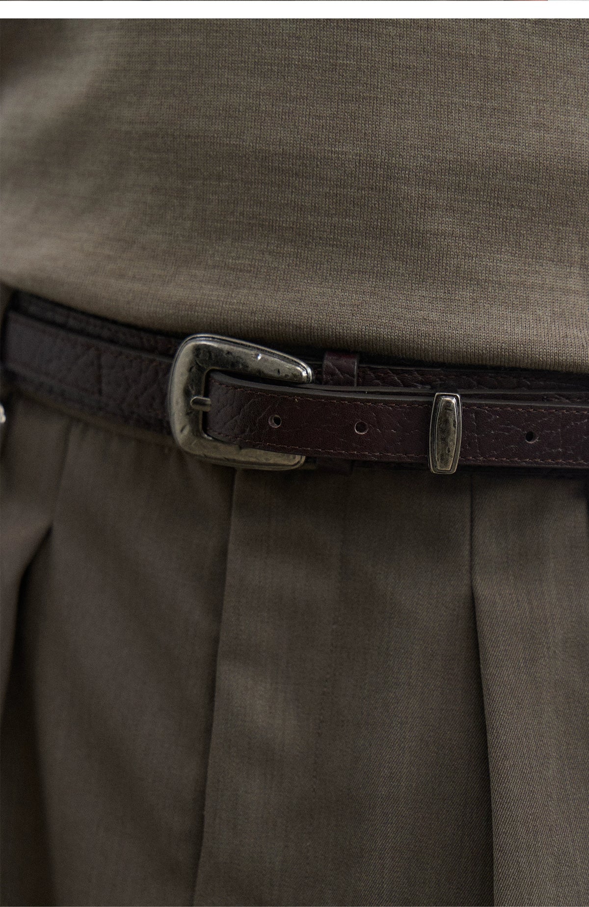 Close-up of the brown textured leather belt's silver pin buckle