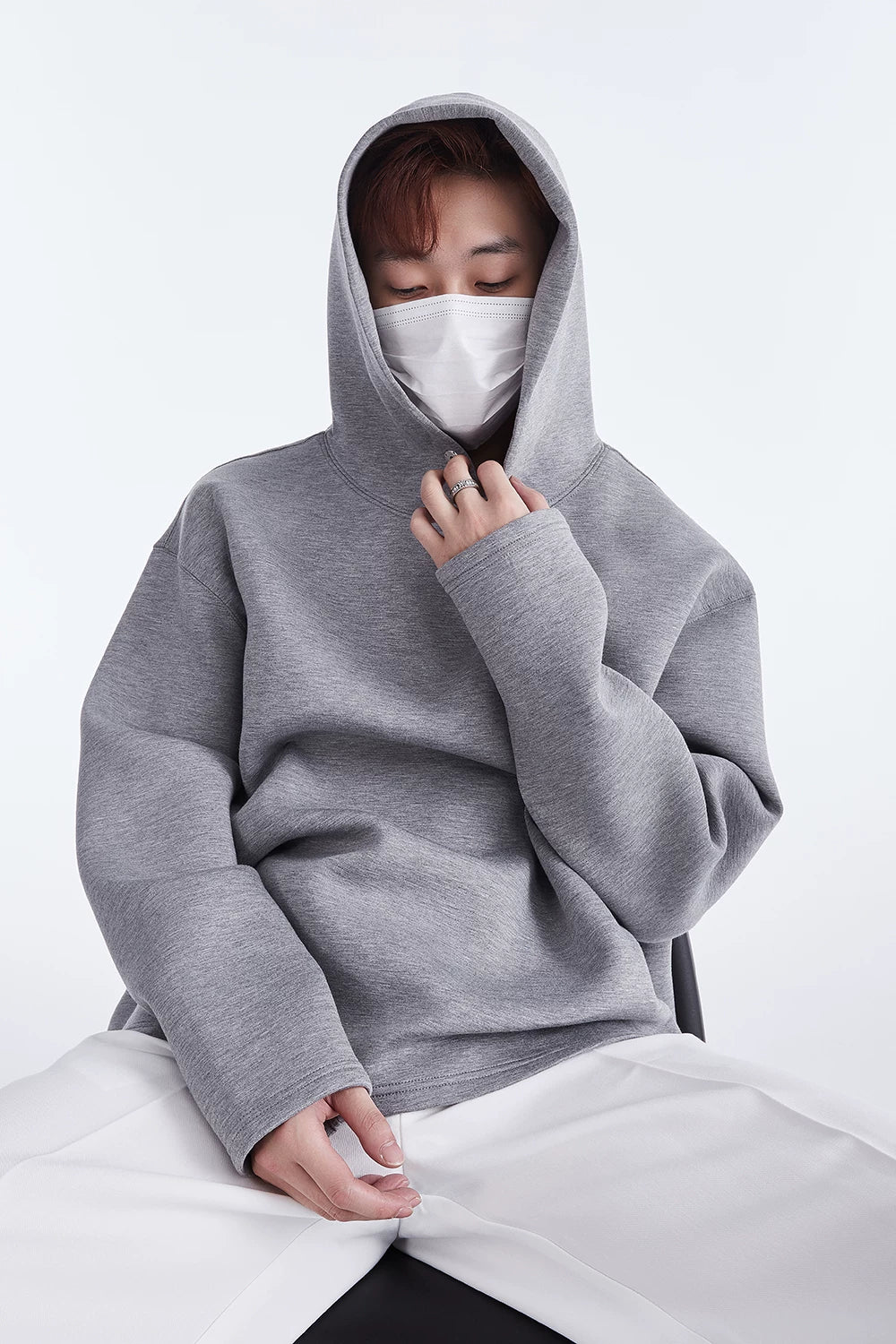 Grey hoodie, seated close front view with hand at neckline