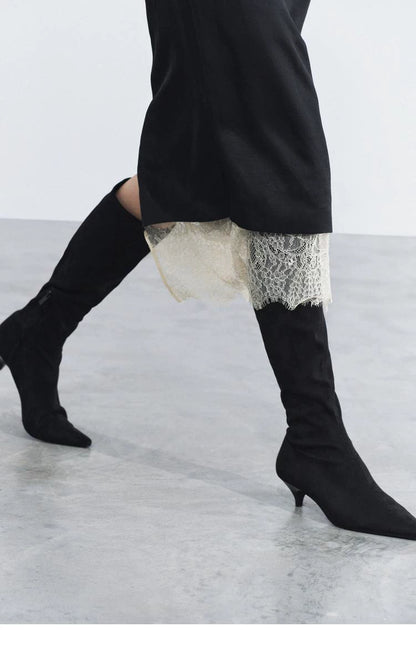 Black pointed-toe kitten-heel boots worn beneath a black lace-trimmed skirt