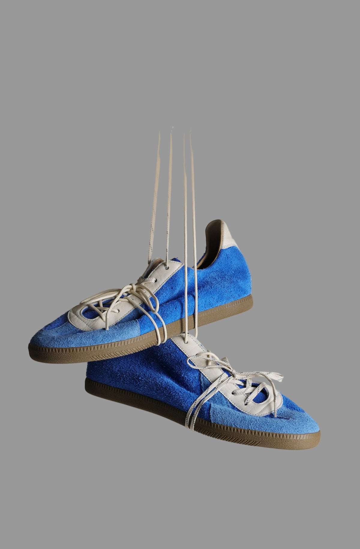 Blue Vintage German Sneakers hanging by their laces against a gray background