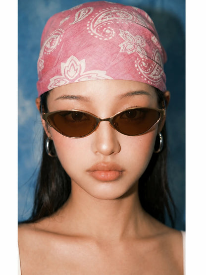 Model wearing gold-tone cat-eye sunglasses with brown lenses and a pink bandana