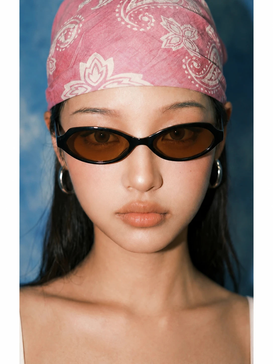 Front portrait of a model wearing black rounded-square sunglasses with brown lenses and a pink bandana.