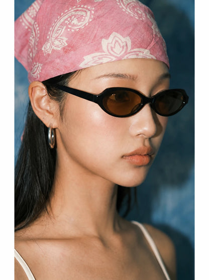 Side portrait of a model wearing black rounded-square sunglasses with brown lenses and a pink bandana.