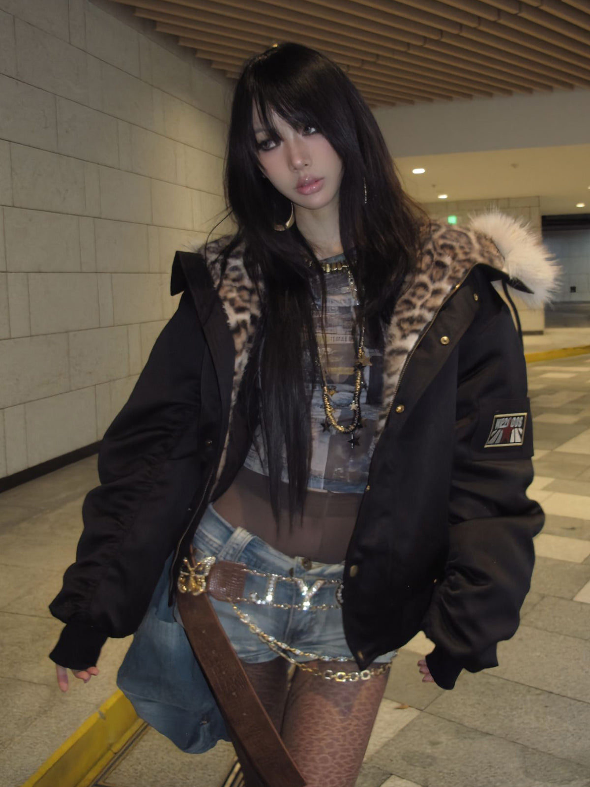Model wearing a black streetwear bomber jacket open over a patterned top and denim shorts