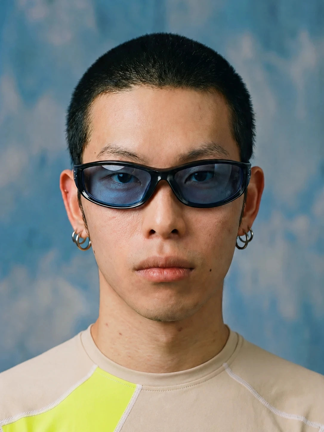 Model wearing black wraparound sunglasses with blue lenses against a blue background.