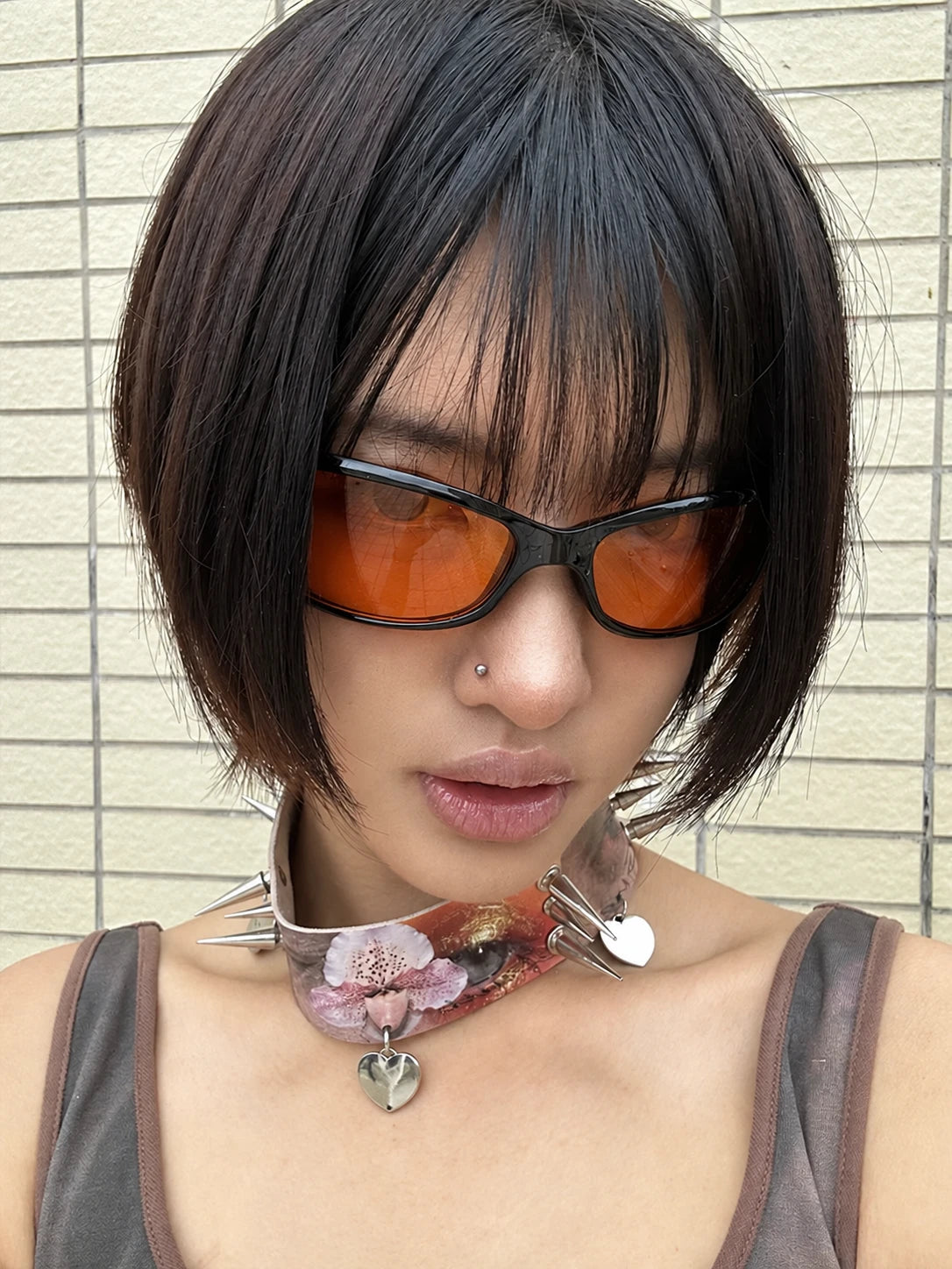 Model wearing black wraparound sunglasses with orange lenses in front of a tiled wall.